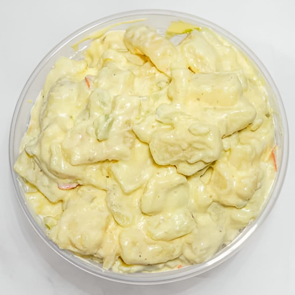 Creamy potato salad with small red and green flecks in a clear plastic container.