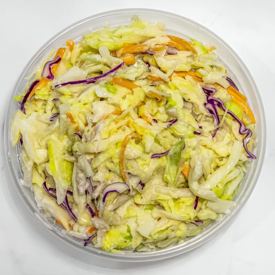 A clear plastic container filled with Baba's Deli Subs coleslaw, featuring shredded cabbage, carrots, and red onion.