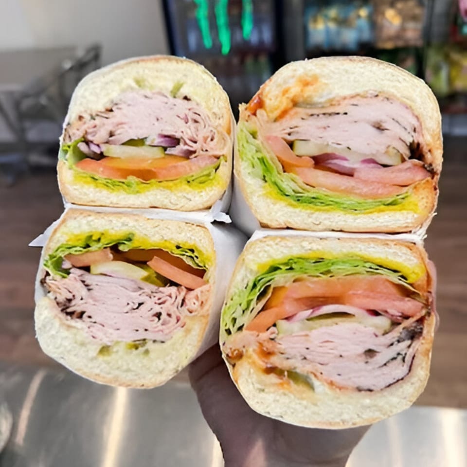 Four halves of Baba's Deli Subs, filled with deli meat, lettuce, tomatoes, and pickles.